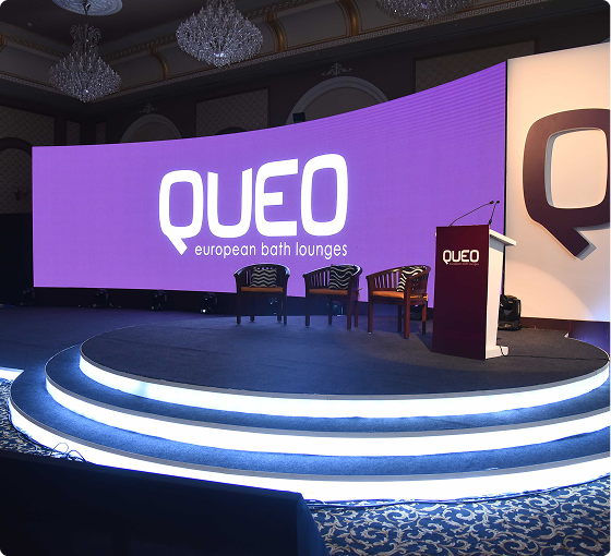 QUEO European Bath Lounges branded stage with curved purple LED wall